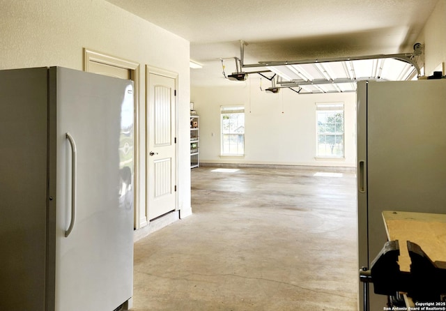 kitchen with concrete flooring, stainless steel refrigerator with ice dispenser, and freestanding refrigerator