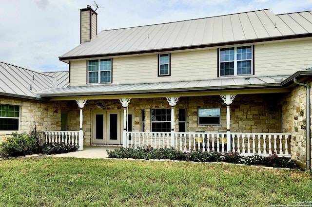 view of front facade featuring metal roof, a porch, stone siding, a standing seam roof, and a chimney