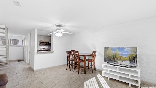 dining space featuring brick wall, baseboards, and a ceiling fan