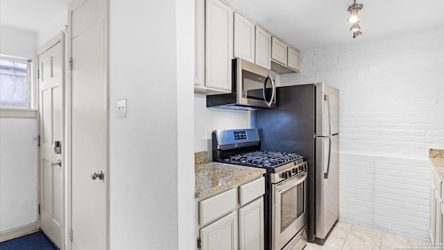 kitchen featuring brick wall, appliances with stainless steel finishes, and light stone counters