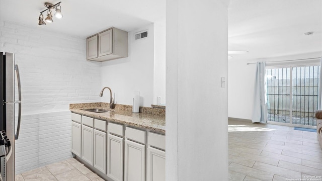 kitchen featuring light stone counters, visible vents, freestanding refrigerator, a sink, and brick wall