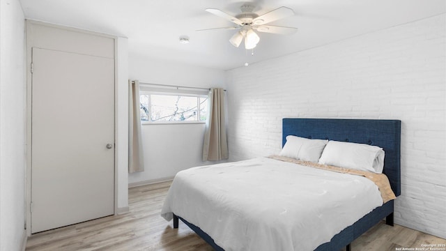 bedroom featuring light wood-type flooring, brick wall, and a ceiling fan