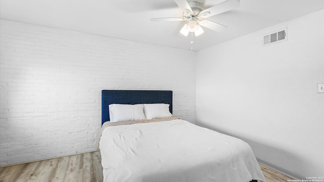 bedroom with visible vents, a fireplace, brick wall, and wood finished floors