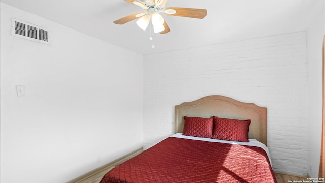 bedroom with brick wall, wood finished floors, visible vents, baseboards, and a ceiling fan