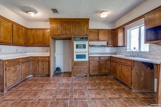 kitchen featuring double oven, brown cabinets, and a sink