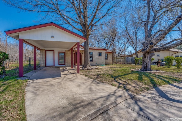 view of front of house with brick siding, concrete driveway, fence, a carport, and a front lawn