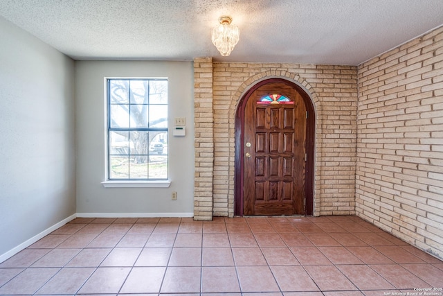 foyer with arched walkways, brick wall, light tile patterned floors, and a textured ceiling