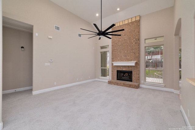 unfurnished living room featuring visible vents, a ceiling fan, light colored carpet, a fireplace, and high vaulted ceiling