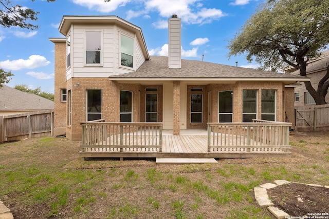 rear view of house featuring a fenced backyard, a chimney, roof with shingles, a wooden deck, and brick siding