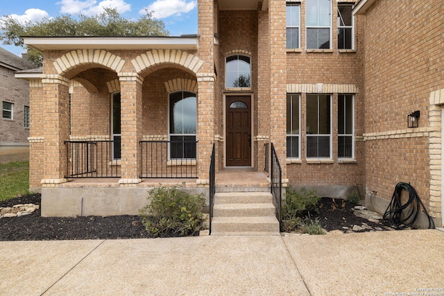 view of exterior entry featuring covered porch and brick siding