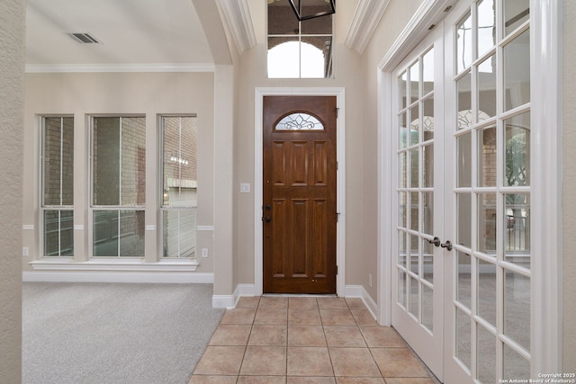 foyer entrance with french doors, crown molding, light tile patterned floors, visible vents, and light carpet