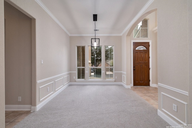 carpeted foyer entrance with ornamental molding, wainscoting, tile patterned floors, and a decorative wall