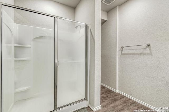 bathroom with visible vents, a textured wall, a shower stall, and wood finished floors