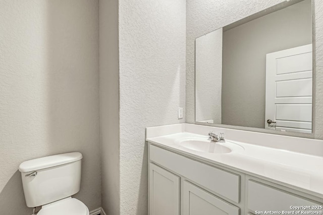 half bathroom with a textured wall, vanity, and toilet