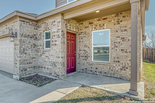 property entrance featuring brick siding, an attached garage, and fence