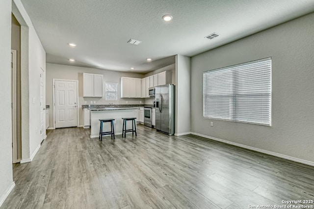 kitchen with visible vents, white cabinets, appliances with stainless steel finishes, wood finished floors, and a center island