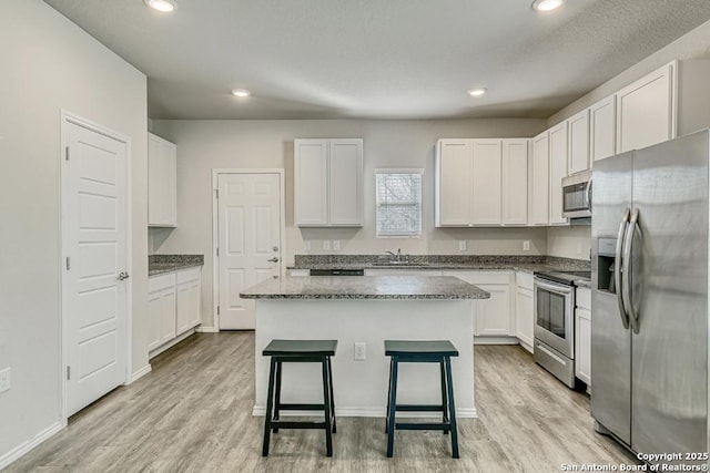 kitchen featuring a center island, stainless steel appliances, white cabinets, a sink, and a kitchen bar