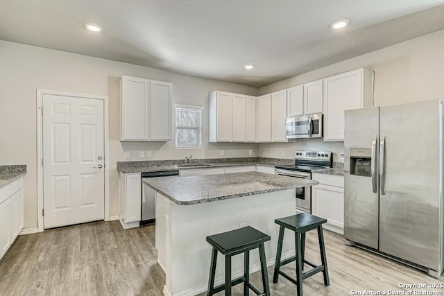 kitchen featuring a kitchen island, appliances with stainless steel finishes, light wood-type flooring, a kitchen bar, and a sink