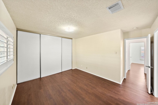 unfurnished bedroom with a closet, visible vents, a textured ceiling, and wood finished floors