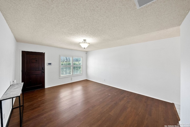 interior space featuring a textured ceiling, dark wood-type flooring, visible vents, and baseboards