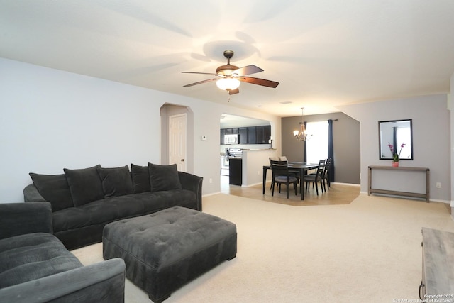 living area featuring light carpet, baseboards, arched walkways, and ceiling fan with notable chandelier