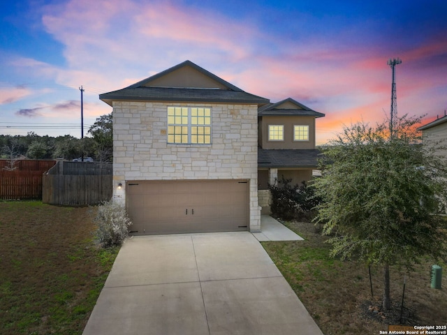 traditional-style home with stone siding, driveway, an attached garage, and fence