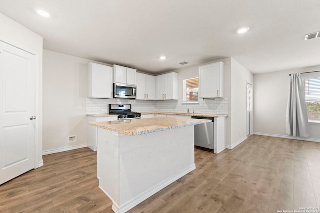 kitchen with light wood finished floors, visible vents, white cabinets, a kitchen island, and appliances with stainless steel finishes