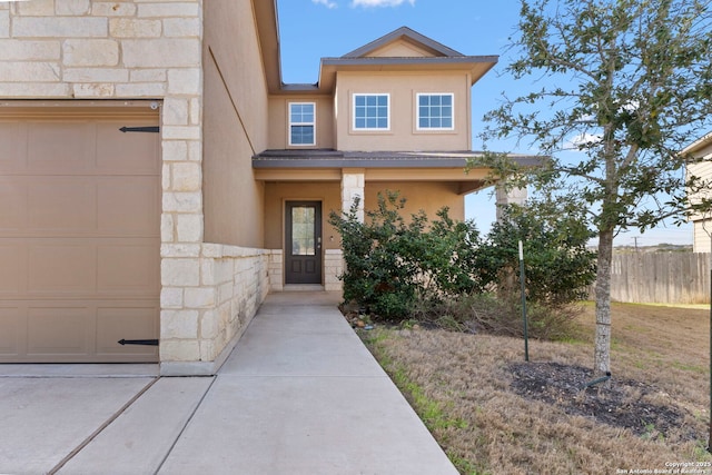 view of front of house with stone siding, fence, an attached garage, and stucco siding