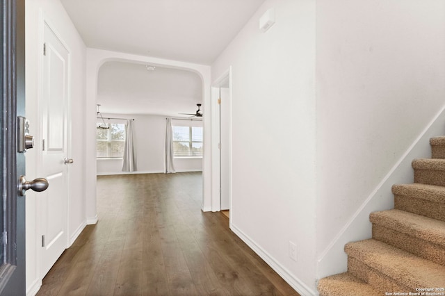 interior space with arched walkways, stairway, dark wood-style flooring, and baseboards