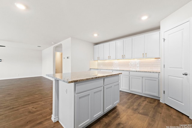 kitchen with arched walkways, tasteful backsplash, dark wood finished floors, and white cabinets