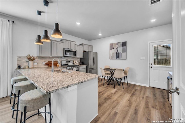 kitchen with a breakfast bar, gray cabinetry, appliances with stainless steel finishes, a sink, and light wood-type flooring