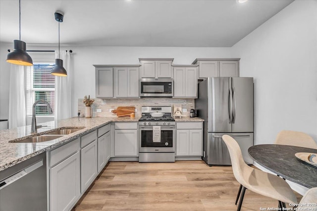 kitchen with stainless steel appliances, tasteful backsplash, gray cabinetry, light wood-style floors, and a sink