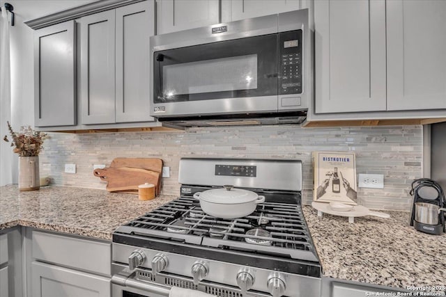 kitchen featuring stainless steel appliances, tasteful backsplash, gray cabinets, and light stone countertops