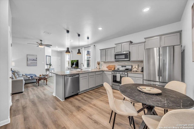 kitchen featuring appliances with stainless steel finishes, a peninsula, gray cabinets, light wood-type flooring, and a sink