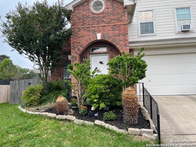 view of exterior entry with a garage, brick siding, cooling unit, and fence