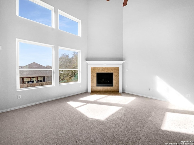 unfurnished living room featuring baseboards, carpet flooring, a towering ceiling, and a tiled fireplace