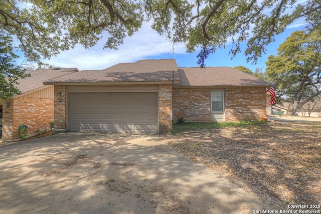 single story home with a garage, concrete driveway, brick siding, and a shingled roof