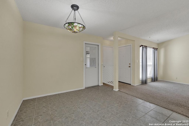 carpeted spare room featuring a textured ceiling and baseboards