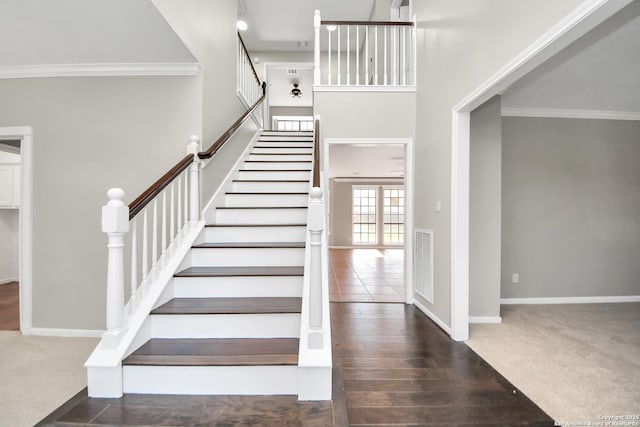 carpeted foyer featuring visible vents, a towering ceiling, stairs, baseboards, and ornamental molding