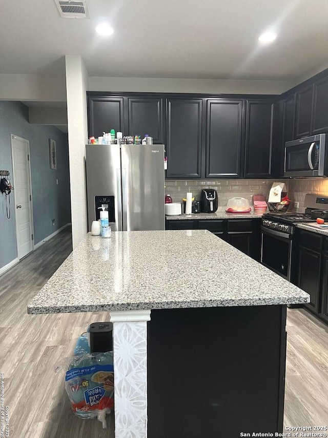 kitchen with light stone counters, a kitchen island, visible vents, appliances with stainless steel finishes, and tasteful backsplash