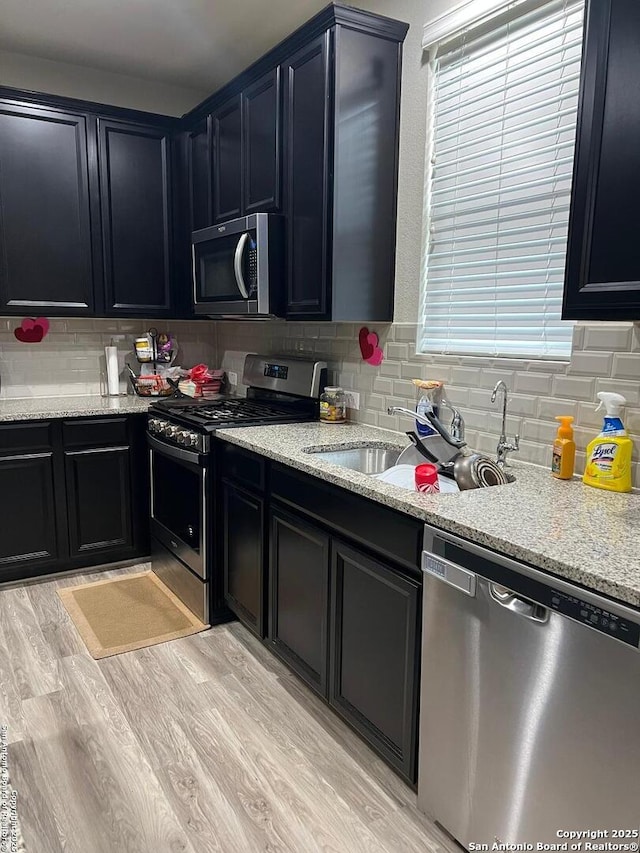 kitchen with decorative backsplash, light wood-style flooring, stainless steel appliances, dark cabinetry, and a sink