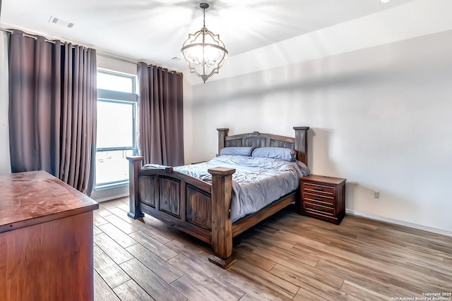 bedroom with baseboards, light wood-style flooring, visible vents, and a notable chandelier