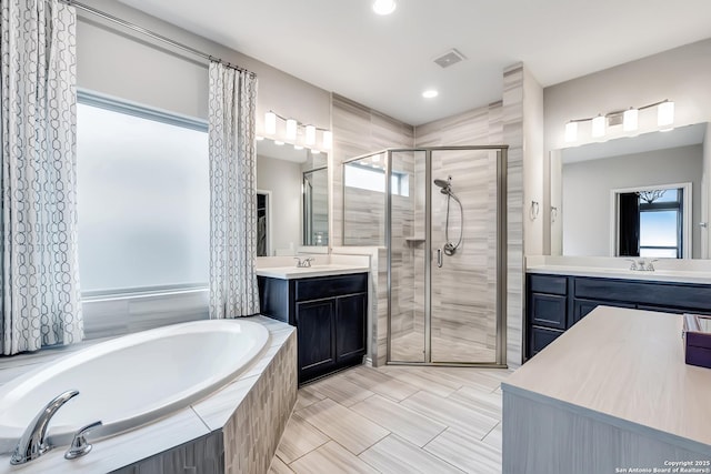 full bathroom with two vanities, visible vents, a stall shower, a sink, and a bath