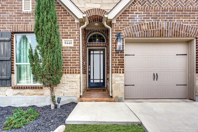 entrance to property with a garage, concrete driveway, brick siding, and stone siding