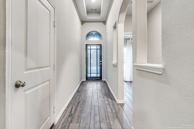 doorway featuring dark wood-style floors, arched walkways, visible vents, a textured wall, and baseboards