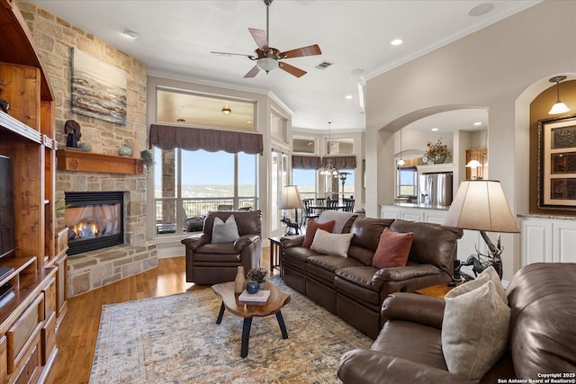 living area featuring crown molding, visible vents, a ceiling fan, a stone fireplace, and wood finished floors