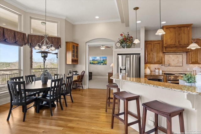 kitchen with arched walkways, brown cabinetry, a kitchen breakfast bar, stainless steel appliances, and backsplash