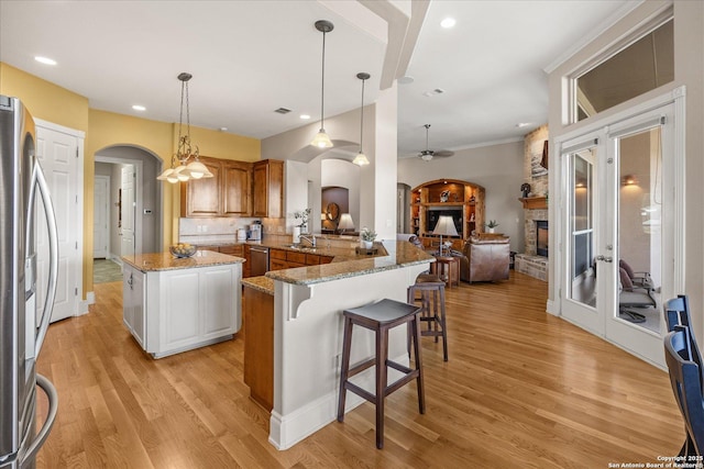 kitchen featuring arched walkways, stainless steel refrigerator with ice dispenser, brown cabinetry, a sink, and a stone fireplace