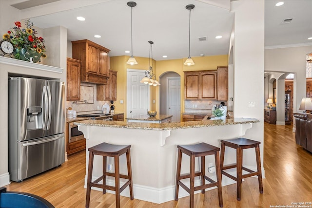 kitchen with arched walkways, stainless steel fridge with ice dispenser, brown cabinets, a peninsula, and light wood-style floors