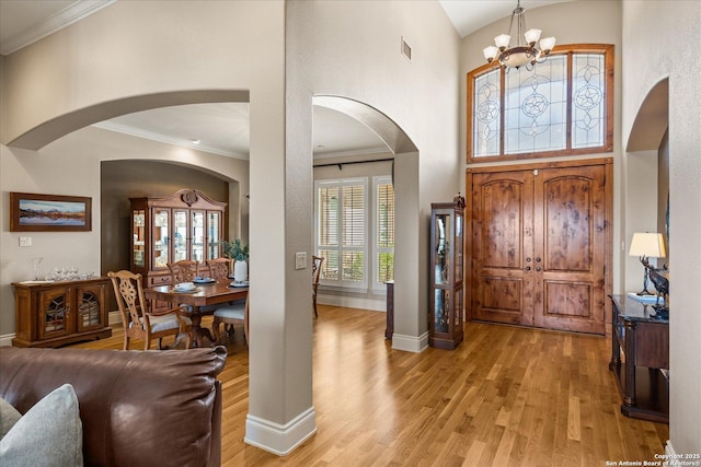 foyer featuring ornamental molding, baseboards, a towering ceiling, and light wood finished floors